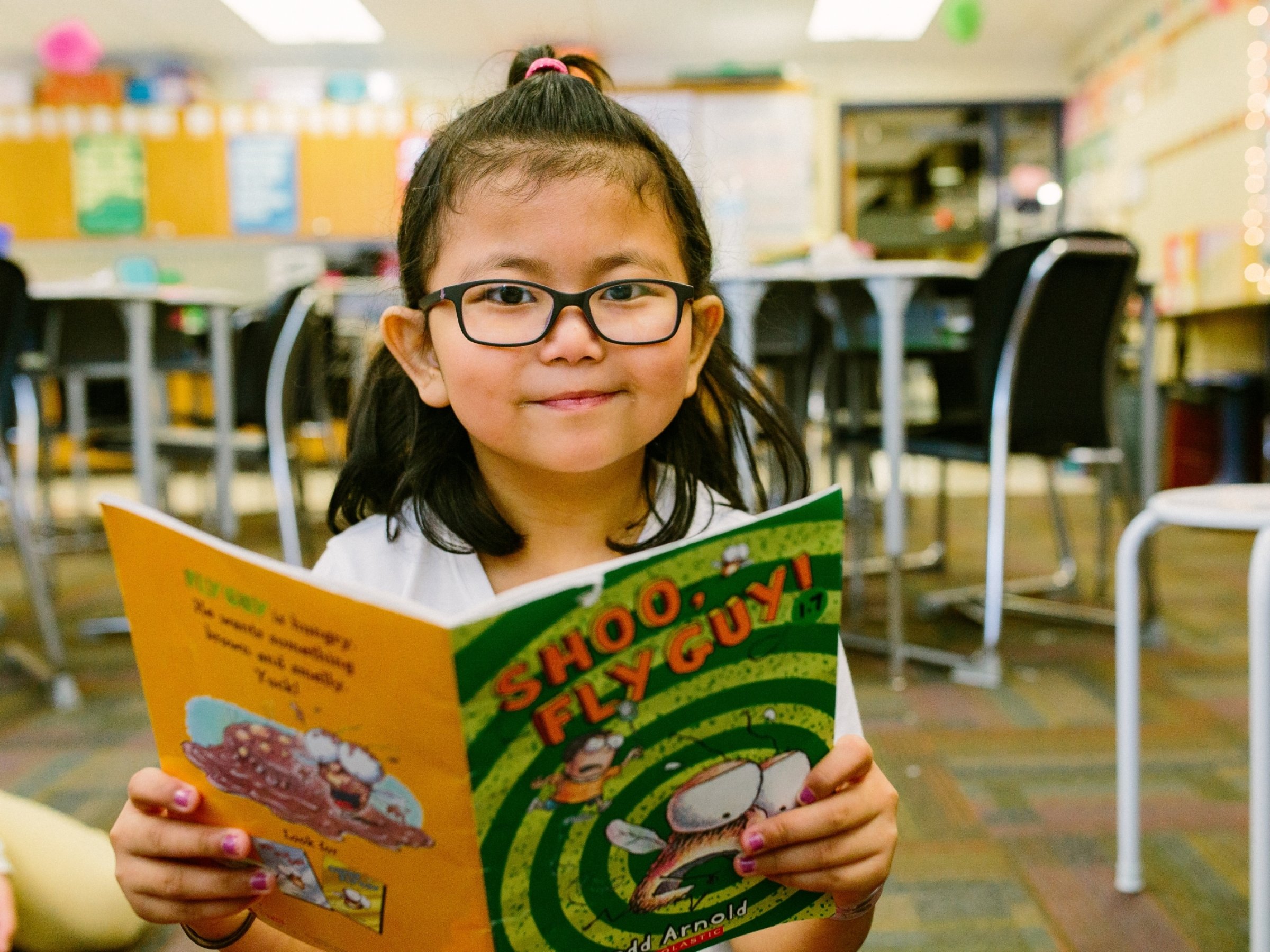 girl with glasses smiling while reading book