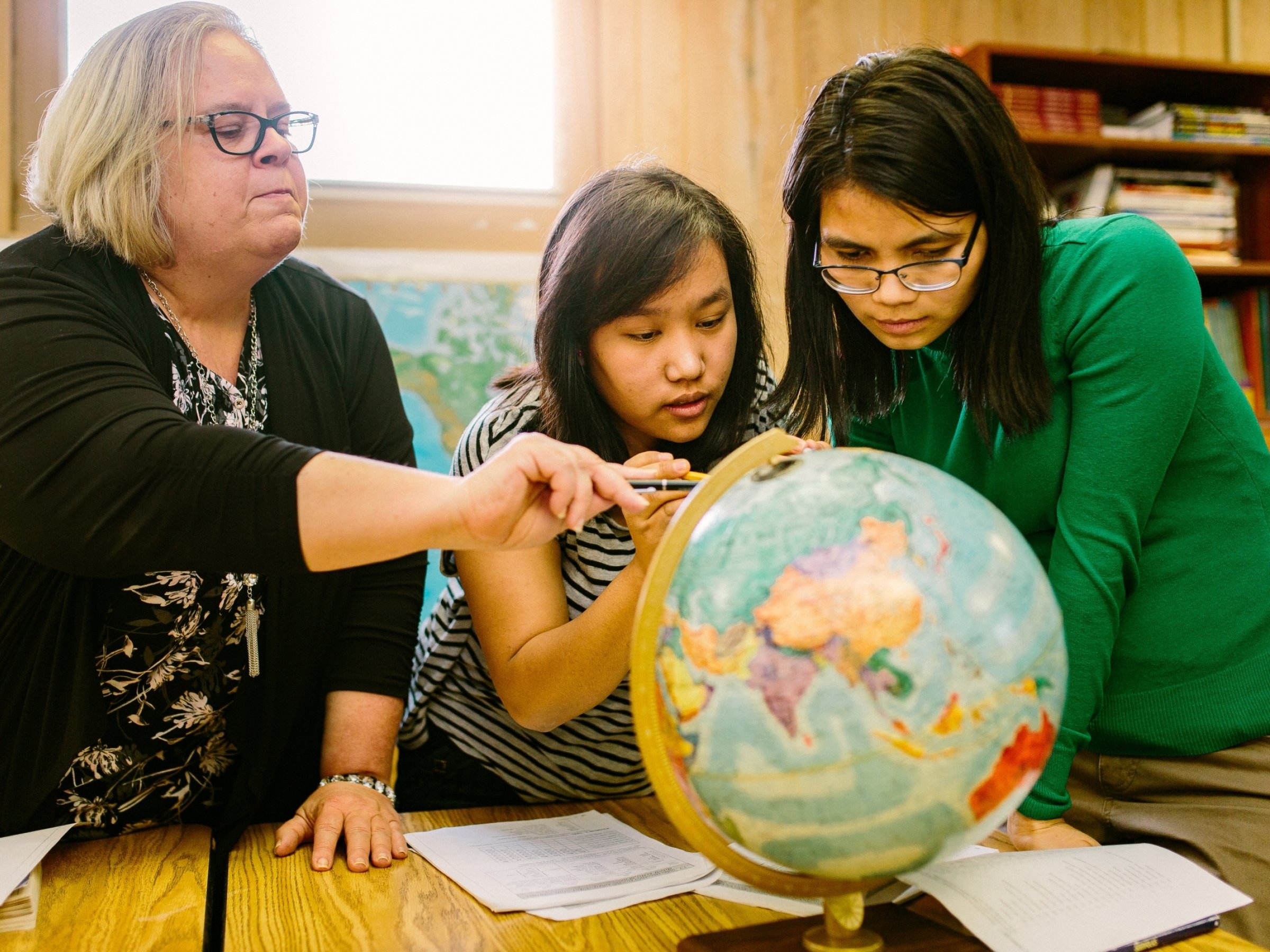 two women and teacher pointing at globe