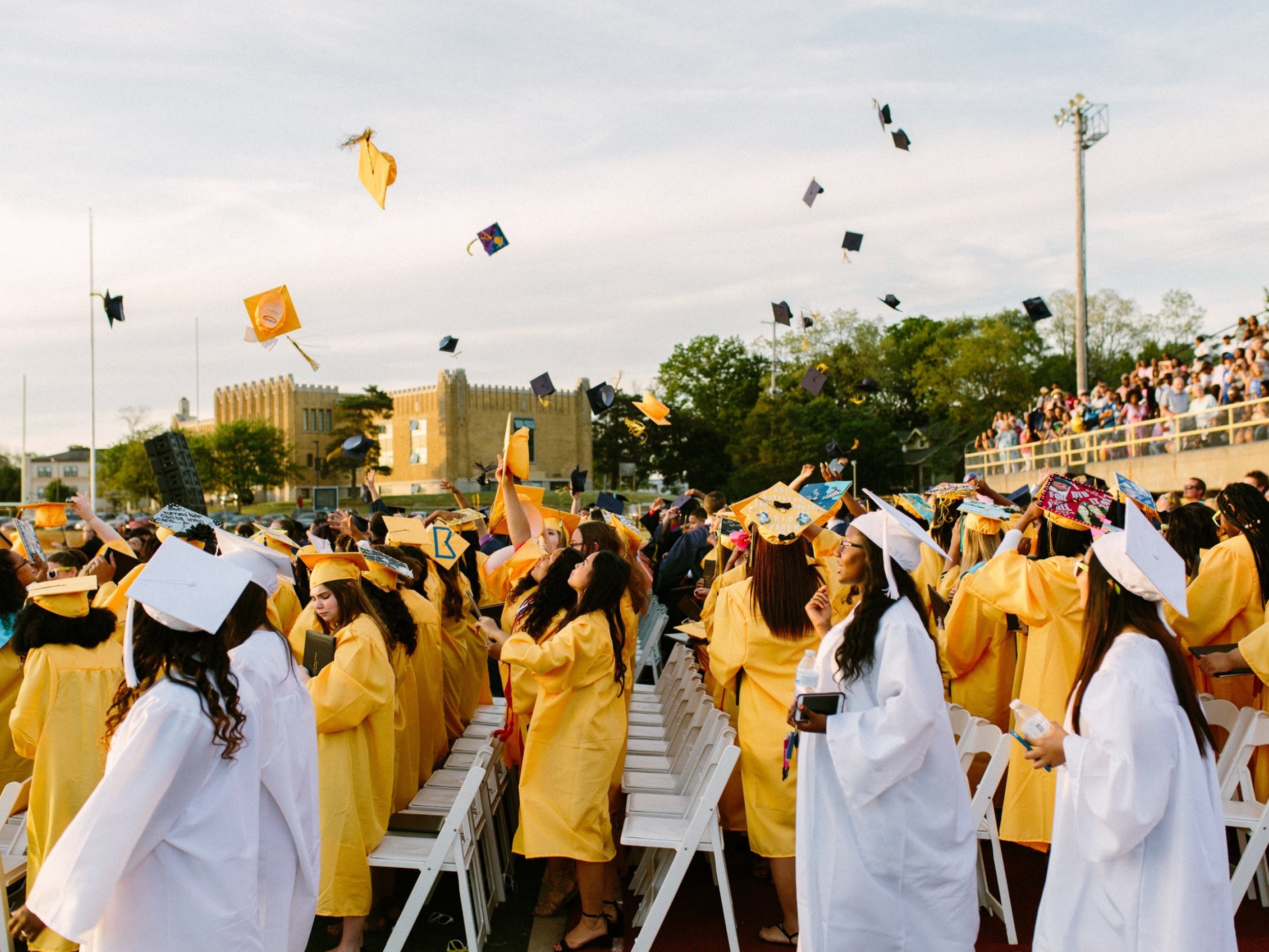 Graduation ceremony with students in yellow and white cap and gown, throwing caps into the air in celebration.